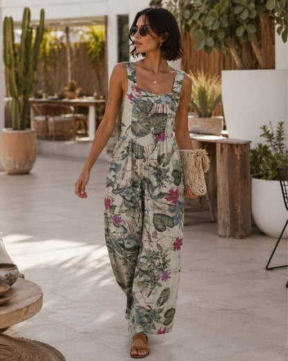 Model trägt einen ärmellosen Damen Jumpsuit mit tropischem Blumenmuster und weitem Bein in mediterraner Sommerkulisse.
