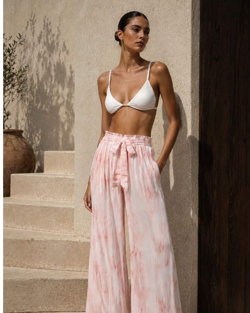 Model trägt eine rosa Damen Palazzo Hose mit Batikmuster, hohem Bund und Bindegürtel kombiniert mit einem weißen Bikini Top im Sommerlook.
