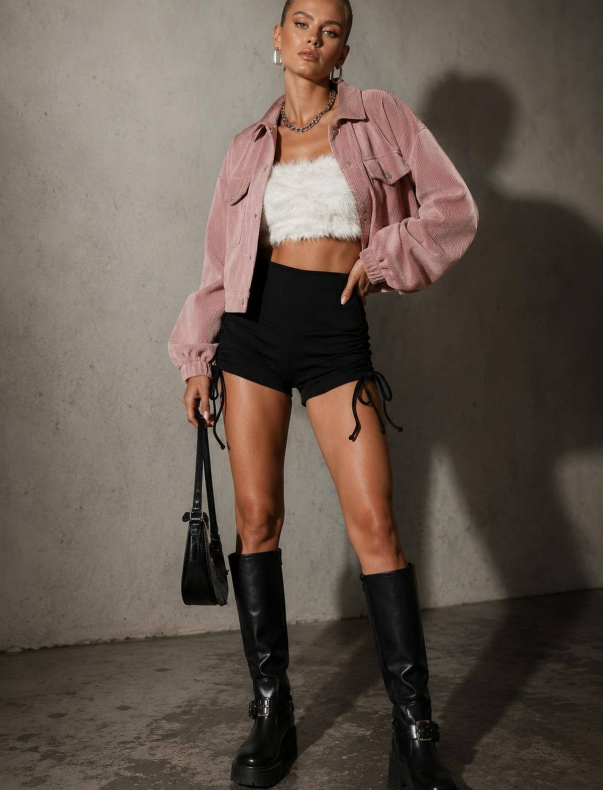 Damen Rebel Herbst Outfit mit rosa Cordjacke, weißem Crop Top, schwarzen Shorts mit seitlicher Schnürung und schwarzen Stiefeln